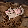 newborn, baby, sleeping, knitted_hat, crocheted_toy, teddy_bear, wrapped_baby, bowl, brown_blanket, wooden_floor, peaceful, cute, infant, soft_texture, cozy, portrait, child, indoors, warm_colors, resting