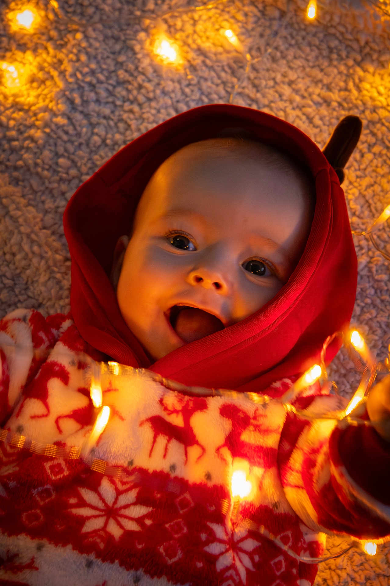 Aëdan a rejoint le concours — aidez-le/la à gagner de superbes lots ! baby, carpet, child, closeup, cozy, cute, face, fairy_lights, festive_sweater, happy, holiday_theme, indoors, infant, playful, portrait, red_hood, reindeer_pattern, smiling, warm_lighting, winter_clothing