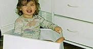 Marianna is registered to the contest to win money with this photo: child, girl, toddler, smiling, happy, portrait, indoors, bedroom, dresser, drawer, furniture, white_furniture, wooden_floor, long_sleeves, clothing, brown_hair, curly_hair, sitting, playful, home
