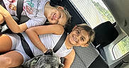King is registered to the contest to win money with this photo: child, children, dog, car, seatbelt, car_seat, smile, happy, pet, animal, backseat, window, road, travel, friendship, casual_clothing, summer, daytime, interior, family