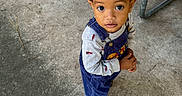 Alex is registered to the contest to win money with this photo: toddler, child, portrait, standing, looking_at_camera, wide_eyes, curly_hair, smiling, outdoor, concrete, picnic_table, bench, sandals, overalls, shirt, blue_clothing, playground, photography, full_body, orange_finger