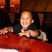 Dexter joined the competition — help win amazing prizes! toddler, child, smiling, happy, table, restaurant, indoor, booth, furniture, person, black_shirt, high_chair, lighting, face, hands, joy, cute, baby, seat, hair