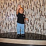 child, toddler, smiling, waving, standing, portrait, indoor, tile_wall, geometric, pattern, reflection, shiny_floor, black_shirt, jeans, shoes, happy, laughing, full_body, lobby, architecture