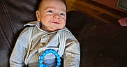 Liam joined the competition — help win amazing prizes! baby, blue_eyes, child, clothing, cute, drool, furniture, happy, indoor, infant, leather_couch, pants, person, portrait, relaxing, shirt, smile, suspenders, teething_toy, young
