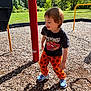 child, toddler, playing, outdoor, playground, sunny, grass, trees, woodchips, clothing, pants, shirt, sneakers, smiling, happy, daylight, fun, person, active, recreation