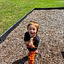 Uhtred is registered to the contest to win money with this photo: child, laughing, playground, wood_chips, grass, trees, orange_pants, pumpkin_pattern, sneakers, black_tshirt, outdoor, daylight, happy, person, fun, nature, smile, young, casual_clothing, sunny