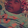baby, child, infant, bonnet, flower_pattern, clothing, sleepy, face, portrait, lying_down, blanket, cozy, cute, indoors, soft_light, person, fabric, headwear, smile, skin