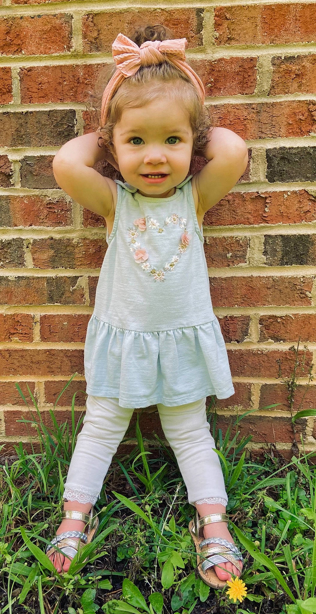 Rylie is registered to the contest to win money with this photo: baby_toddler_clothing, brick, brickwork, cheek, child, eye, face, grass, green, hair, happy, head, iris, people_in_nature, person, pink, plant, skin, sleeve, smile
