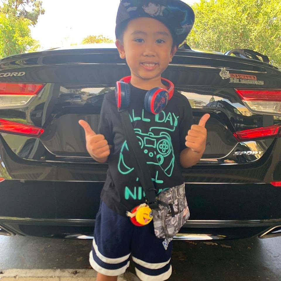 Jo Aizen is registered to the contest to win money with this photo: asphalt, automotive_design, automotive_exterior, automotive_lighting, automotive_tail_brake_light, automotive_tire, bumper, car, cool, headwear, joy, motor_vehicle, parking, person, personal_luxury_car, personal_protective_equipment, t_shirt, tints_and_shades, toddler, tree