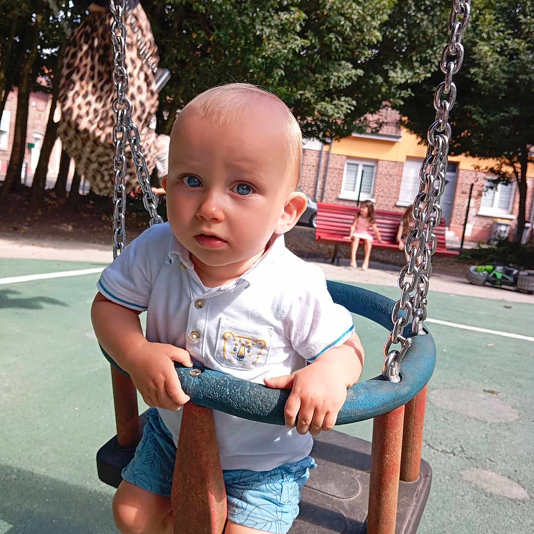 Eliott a rejoint le concours — aidez-le/la à gagner de superbes lots ! bench, blue_eyes, chain, child, curious, daylight, expression, metal, outdoor, park, person, playground, sandals, seat, shorts, summer, swing, toddler, tree, white_shirt