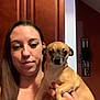Pepper is registered to the contest to win money with this photo: woman, dog, indoor, cabinet, brown_hair, pet, holding, small_dog, tan_dog, face, portrait, home, decor, sign, hand, casual, expression, person, animal, furniture