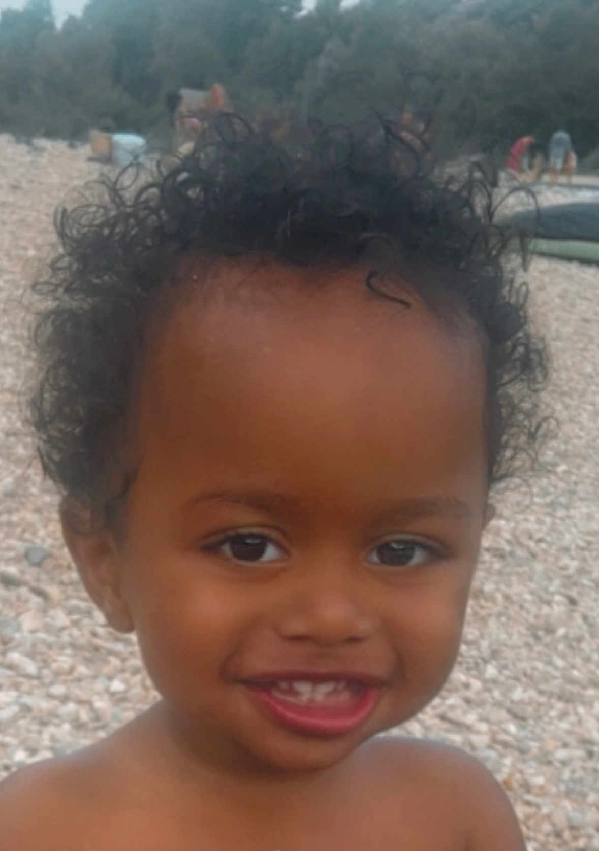 Naïm participe au concours pour gagner de l'argent avec cette photo : child, toddler, smile, curly_hair, outdoor, beach, pebbles, face, happy, portrait, skin, person, nature, daylight, expression, young, cute, bare_shoulders, vacation, childhood