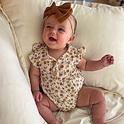 Hallie joined the competition — help win amazing prizes! baby, infant, smiling, headband, bow, floral_clothing, romper, couch, cream_color, indoor, happy, cute, child, person, skin, legs, hand, seated, portrait, cozy