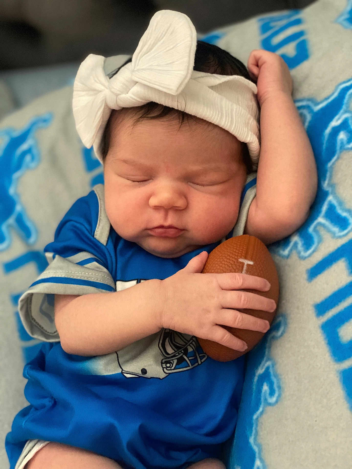 Mariana is registered to the contest to win money with this photo: baby, sleeping, blue_clothing, headband, football, toy, blanket, infant, cute, peaceful, child, resting, hand, face, portrait, indoor, soft_texture, comfort, young, closeup