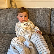 Arié participe au concours pour gagner de l'argent avec cette photo : baby, blanket, blue_eyes, cheeks, child, couch, cozy, curious_expression, face, furniture, hair, head, indoor, pajamas, person, relaxed, sitting, skin, striped_clothing, young_child