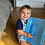 Arié a rejoint le concours — aidez-le/la à gagner de superbes lots ! baby, blue_eyes, casual_clothing, child, couch, cute, face, floor, furniture, happy, home, indoor, overalls, person, plastic_lid, playful, short_hair, smiling, toddler, wooden_floor