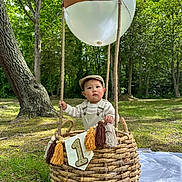 Parvin joined the competition — help win amazing prizes! baby, child, basket, balloon, crown, first_birthday, outdoor, forest, grass, picnic_blanket, overalls, hat, tassels, sunlight, nature, celebration, portrait, cute, one_year_old, infant