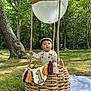 baby, child, basket, balloon, crown, first_birthday, outdoor, forest, grass, picnic_blanket, overalls, hat, tassels, sunlight, nature, celebration, portrait, cute, one_year_old, infant