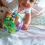 Rose participe au concours pour gagner de l'argent avec cette photo : baby, infant, child, onesie, toy, ball, dinosaur, bed, blanket, playful, cute, indoors, person, smiling, hand, face, head, lying_down, colorful, soft