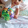 baby, infant, child, onesie, toy, ball, dinosaur, bed, blanket, playful, cute, indoors, person, smiling, hand, face, head, lying_down, colorful, soft
