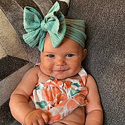 Skylar is registered to the contest to win money with this photo: baby, child, smiling, headband, bow, couch, fabric, clothing, floral, pattern, cute, portrait, skin, hand, sitting, indoors, cheeks, eyes, baby_clothes, comfort