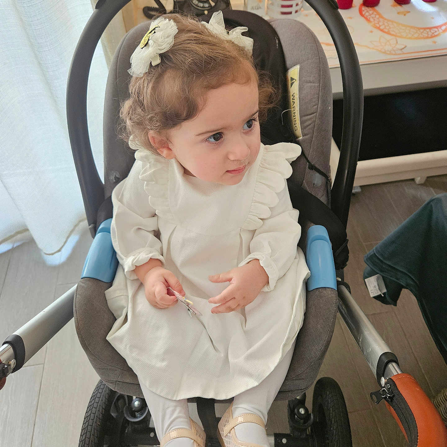 Séréna participe au concours pour gagner de l'argent avec cette photo : toddler, child, stroller, white_dress, curly_hair, hair_bows, indoor, floor, candles, curtains, window, footwear, baby_shoes, hand, face, person, seat, car_seat, home, furniture