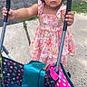 toddler, child, girl, curly_hair, bow, floral_dress, stroller, sidewalk, outdoor, sunlight, grass, pavement, pink, white, holding, playful, portrait, summer, baby_bottle, cute