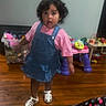 Valerie Alonzo is registered to the contest to win money with this photo: toddler, child, denim_dress, pink_shirt, white_sandals, wooden_floor, toys, indoor, curly_hair, stroller, expression, playroom, plastic_toys, container, furniture, person, young_child, flooring, casual_clothing, standing