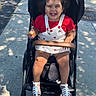 Valerie Alonzo is registered to the contest to win money with this photo: toddler, child, stroller, sidewalk, sunlight, shadow, happy, smile, hair, clothing, red_shirt, white_overalls, sandals, food, outdoor, urban, daytime, cute, person, baby