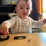 Charly participe au concours pour gagner de l'argent avec cette photo : baby, child, table, bib, indoor, curious, expression, face, person, clothing, arm, wood, furniture, light, window, blurred_background, sitting, young, cute, home