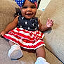 Journee is registered to the contest to win money with this photo: baby, child, smiling, couch, indoor, dress, headwear, bow, white_shoes, socks, happy, person, infant, stars, stripes, red, white, blue, portrait, seated