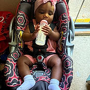 Journee joined the competition — help win amazing prizes! baby, child, car_seat, bottle, milk, pink_headband, bow, socks, indoors, floor, door, window, seat_belt, patterned_fabric, infant, person, cute, feeding, holding, secured