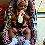 baby, child, car_seat, bottle, milk, pink_headband, bow, socks, indoors, floor, door, window, seat_belt, patterned_fabric, infant, person, cute, feeding, holding, secured