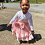 child, girl, smiling, dress, pink, bow, cardigan, braids, beads, outdoor, sidewalk, sunny, shadow, neighborhood, house, grass, cars, happy, person, portrait