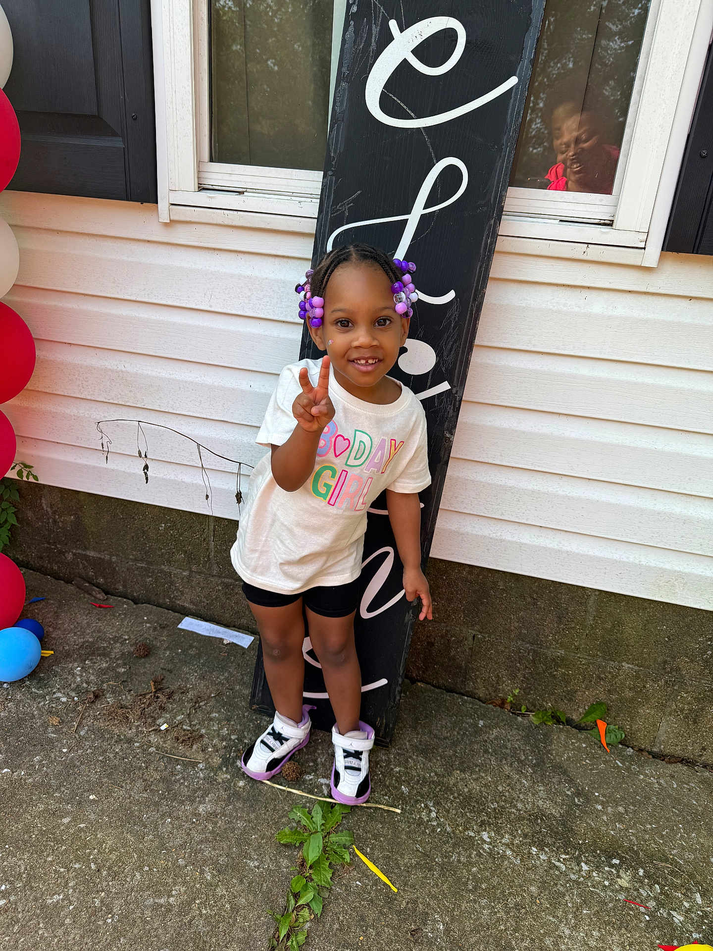 Kyrah joined the competition — help win amazing prizes! child, birthday, girl, peace_sign, purple_beads, sneakers, window, reflection, outdoor, concrete, sign, white_shirt, black_shorts, smiling, person, celebration, balloons, plants, hair_beads, casual_clothing