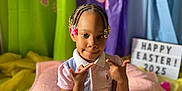 Kyrah joined the competition — help win amazing prizes! beads, braided_hair, child, colorful, curtains, decorations, easter_eggs, gold_egg, indoor, lightbox_sign, pajama_shirt, paw_prints, pink_blanket, pink_eggs, playful_pose, portrait, purple_eggs, smiling, white_shorts, yellow_eggs