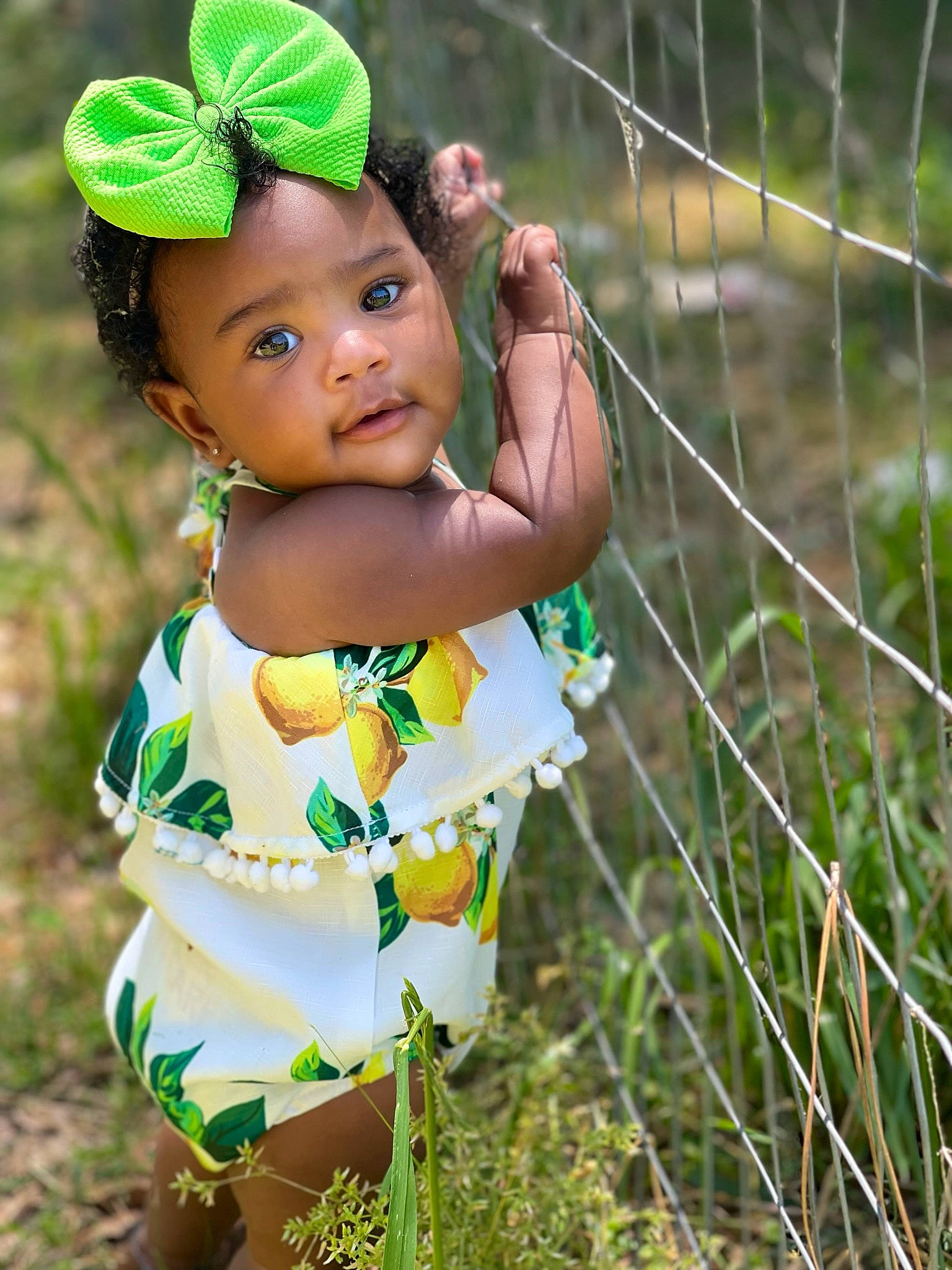 Emani joined the competition — help win amazing prizes! baby, baby_toddler_clothing, child, day_dress, dress, eye, fence, fun, grass, grassland, happy, head, headwear, human_body, mesh, people_in_nature, person, plant, skin, toddler
