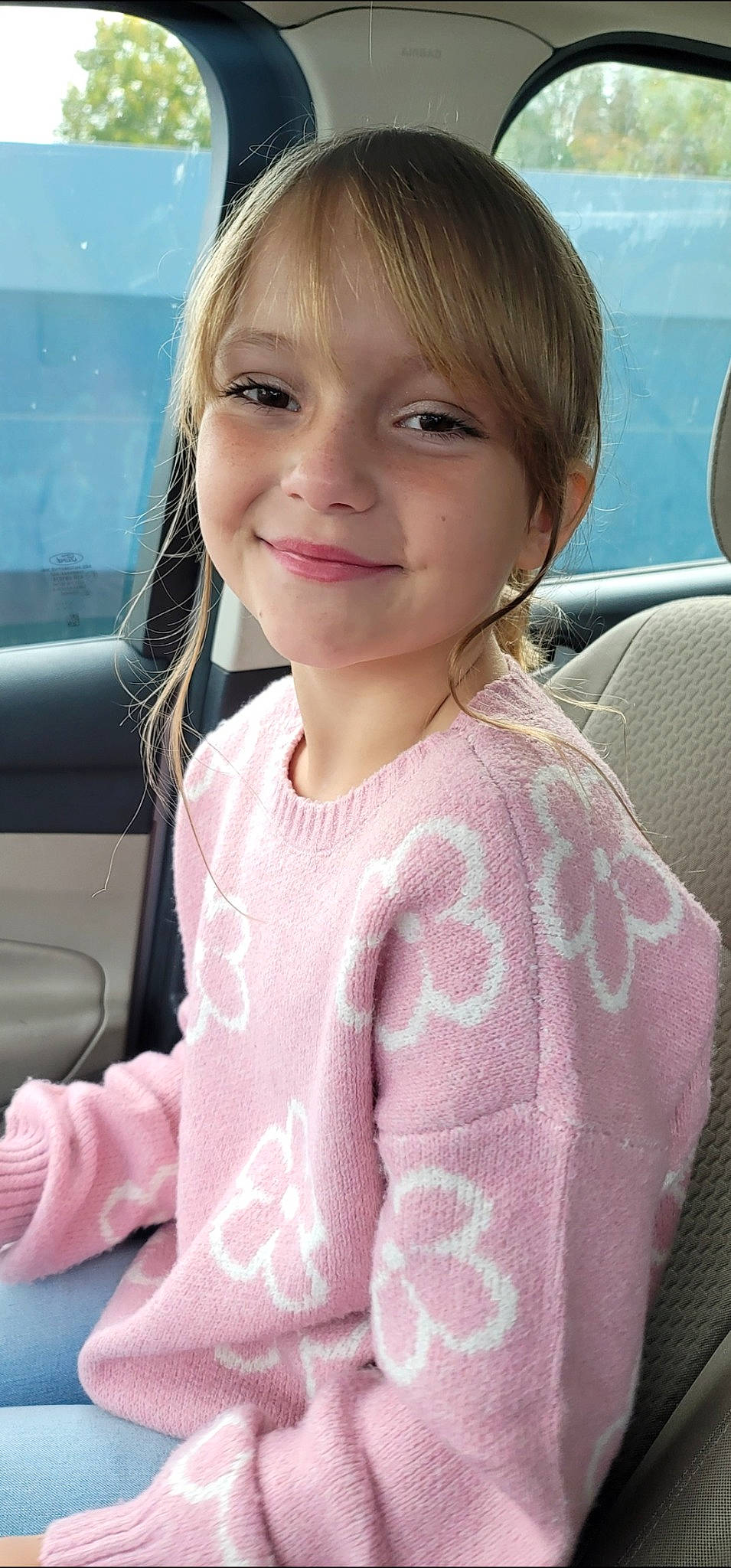 Emily is registered to the contest to win money with this photo: bangs, blond, child, chin, eyebrow, face, facial_expression, hairstyle, happy, head, iris, joy, lip, long_hair, motor_vehicle, person, pink, skin, sleeve, smile