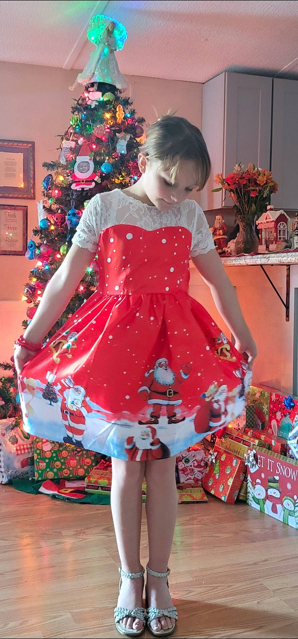 Emily is registered to the contest to win money with this photo: baby_toddler_clothing, christmas, christmas_decoration, christmas_ornament, christmas_tree, day_dress, dress, event, fashion_design, formal_wear, human_leg, one_piece_garment, ornament, pattern, person, red, sleeve, standing, thigh, toddler