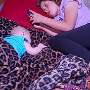 Nathan is registered to the contest to win money with this photo: child, baby, bed, blanket, leopard_print, pillow, curtain, phone, purple_shirt, sleepwear, indoor, relaxing, lying_down, person, furniture, pattern, toddler, family, comfort, casual