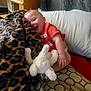 baby, blanket, stuffed_animal, leopard_print, pillow, bedding, bed, smiling, child, indoor, toddler, clothing, red_shirt, furniture, wooden, pattern, cute, happy, soft_toy, relaxed