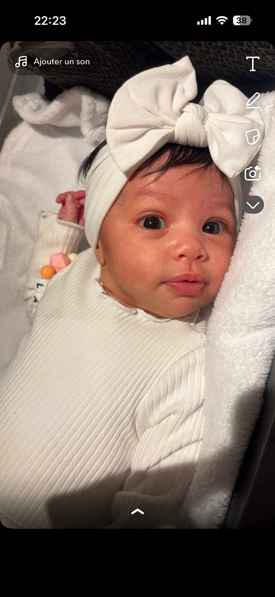 Layana participe au concours pour gagner de l'argent avec cette photo : baby, infant, newborn, headband, bow, white_outfit, ribbed_texture, blanket, towel, beads, bracelet, closeup, portrait, face, eyes, gaze, indoor, soft_light, cozy, crib