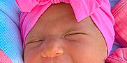 Lydia is registered to the contest to win money with this photo: baby, newborn, pink_bow, headband, pink_clothing, smiling, face, closed_eyes, blanket, outdoor, greenery, infant, cute, portrait, soft_texture, child, headwear, happy, resting, baby_girl