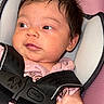 adorable, awake, baby, buckled, car_seat, child, close_up, eyes, face, hair, harness, indoors, infant, photography, pink_background, pink_clothing, portrait, safe, sitting, transportation