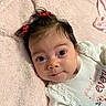 adorable, baby, blanket, child, close_up, clothing, cozy, dark_hair, eyes, face, hair_bows, indoor, infant, lace, onesie, pink_blanket, portrait, red_bows, smiling, wide_eyed
