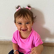 Deniz participe au concours pour gagner de l'argent avec cette photo : toddler, child, smiling, pink_shirt, hair_bows, bracelet, sitting, floor, wooden_floor, happy, indoors, person, cute, face, young_child, casual_clothing, baby, portrait, front_view, wall