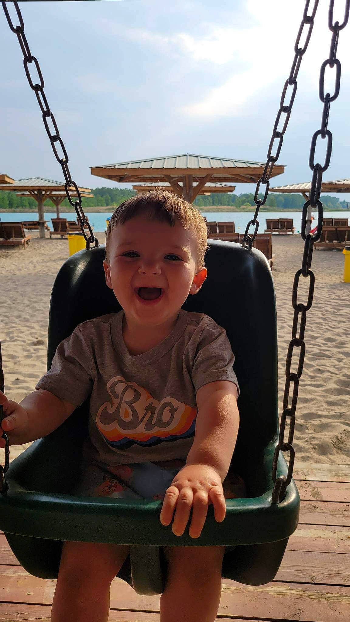 Kamden is registered to the contest to win money with this photo: black, chin, city, facial_expression, fun, happy, leisure, organ, person, photograph, playground, public_space, recreation, skin, sky, smile, standing, swing, toddler, water