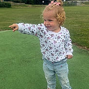 Delilah is registered to the contest to win money with this photo: toddler, child, pointing, curly_hair, pink_bows, white_sweater, polka_dots, cartoon_characters, light_blue_jeans, crocs, outdoor, green_field, grass, trees, basketball_court, daylight, smiling, happy, playful, casual_clothing