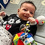 baby, infant, smile, mickey_mouse, toy, colorful, playmat, clothing, happy, child, cute, patterned, soft_toy, lying_down, indoor, face, hand, bright_colors, small_child, portrait