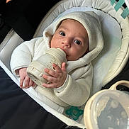 Lyvaï participe au concours pour gagner de l'argent avec cette photo : baby, bottle, hoodie, knitwear, infant, pacifier, seat, soft_toy, white, cream, cute, child, hand, face, indoors, portrait, feeding, newborn, cozy, comfortable